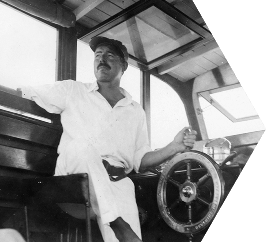 Black and white photo of Ernest Hemingway steering a boat