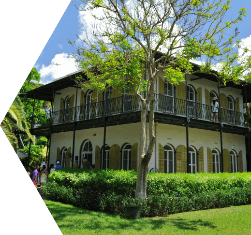 An askance view of the front of the Spanish Colonial two-story villa known as the Ernest Hemingway House in Key West, FL