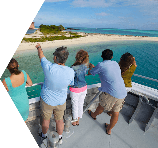 A middle-aged man flanked by two other women facing out towards the Dry Tortugas National Park from the deck of the Yankee Freedom