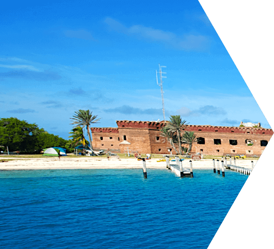 A view of Dinghy Beach in the Dry Tortugas from the water where you can see Ft. Jefferson, dock moorings, palm trees and a sandy beach