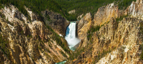 A waterfall surrounded by steep rocky mountains and lush wilderness in Yellowstone National Park