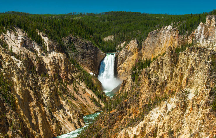 A waterfall surrounded by steep rocky mountains and lush wilderness in Yellowstone National Park